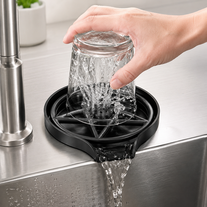 Hand pressing a glass onto a black ABS glass rinser, showing upward water spray inside the cup and drainage flowing into the kitchen sink.